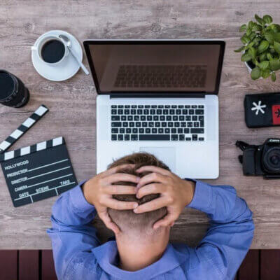 Mann fässt sich verzweifelt an den Hinterkopf mit dem Blick auf Laptop und andere Geräte.